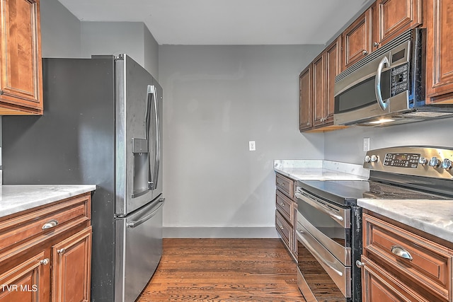 kitchen featuring baseboards, dark wood-style flooring, stainless steel appliances, and brown cabinetry