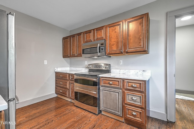 kitchen with brown cabinetry, dark wood finished floors, baseboards, and appliances with stainless steel finishes