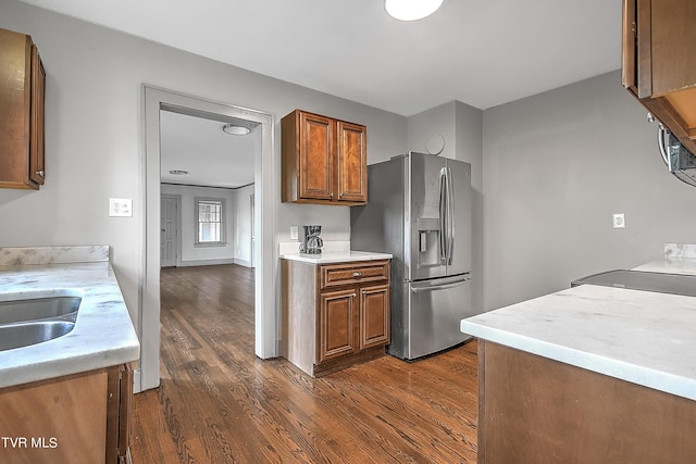 kitchen with dark wood-style flooring, brown cabinetry, stainless steel fridge with ice dispenser, and light countertops