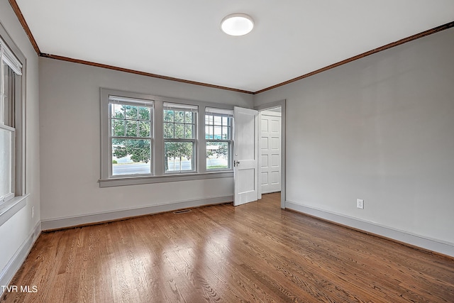 empty room featuring ornamental molding, baseboards, visible vents, and wood finished floors