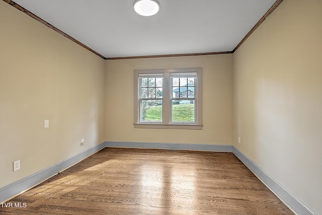 empty room featuring crown molding, baseboards, and wood finished floors