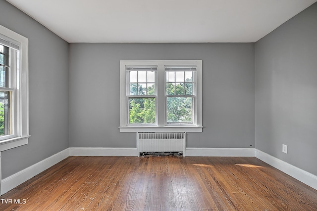 spare room featuring wood finished floors, baseboards, and radiator heating unit