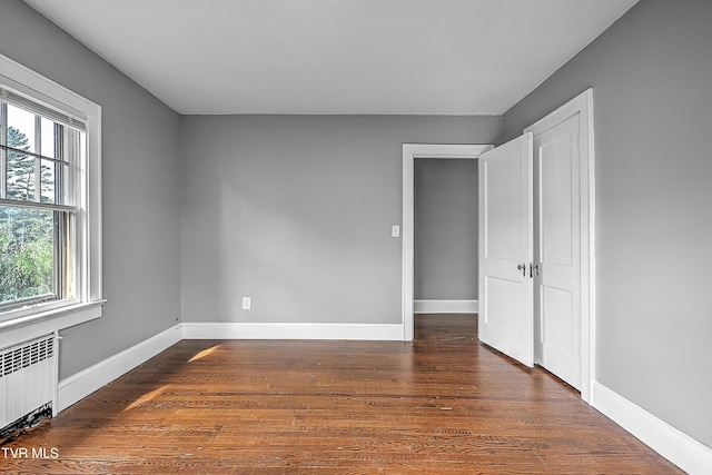unfurnished bedroom featuring baseboards, multiple windows, radiator heating unit, and dark wood-style flooring