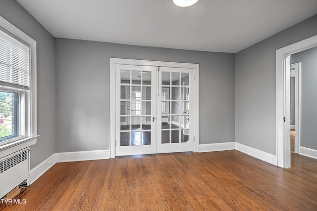 unfurnished room featuring french doors, wood finished floors, baseboards, and radiator heating unit
