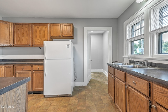 kitchen featuring freestanding refrigerator, brown cabinets, dark countertops, and a sink