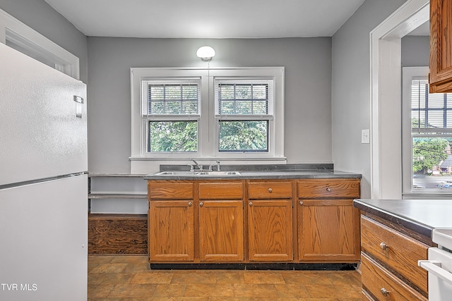 kitchen featuring a sink, brown cabinetry, freestanding refrigerator, range, and dark countertops