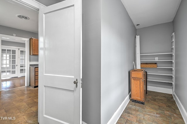 hallway with stone finish flooring, baseboards, and visible vents