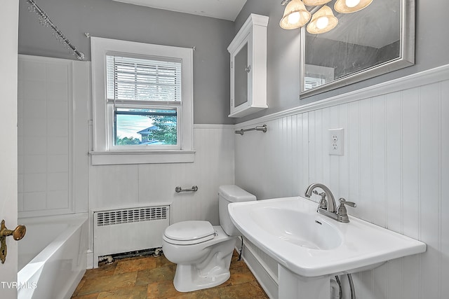 bathroom with a wainscoted wall, toilet, stone finish flooring, and radiator heating unit