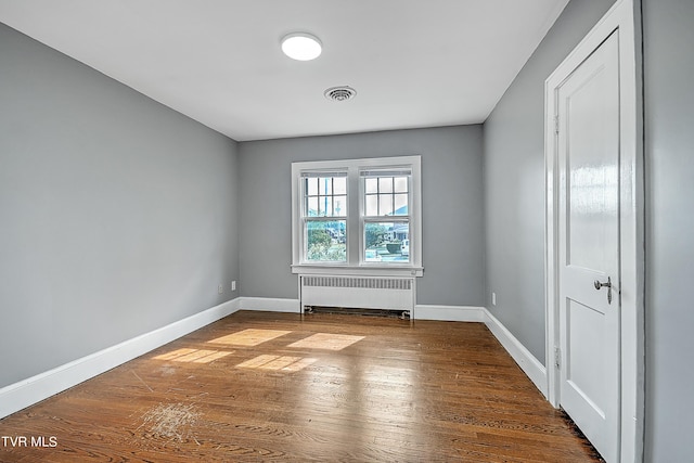spare room featuring visible vents, wood finished floors, baseboards, and radiator heating unit
