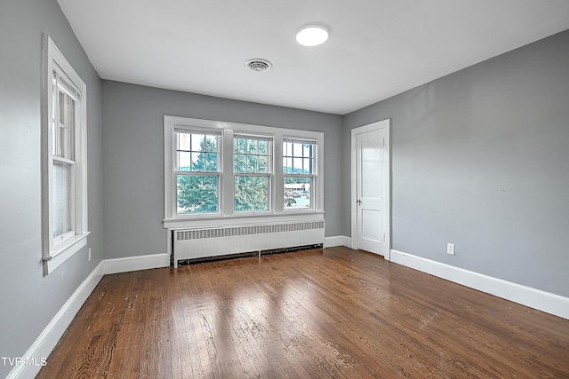 empty room featuring radiator, visible vents, baseboards, and hardwood / wood-style flooring