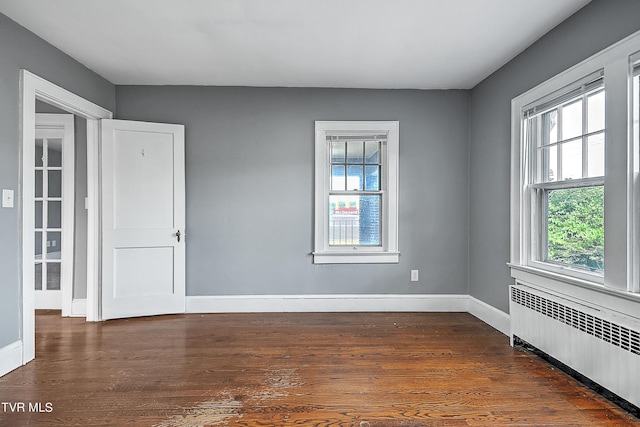 unfurnished room with radiator, a wealth of natural light, baseboards, and dark wood-style floors