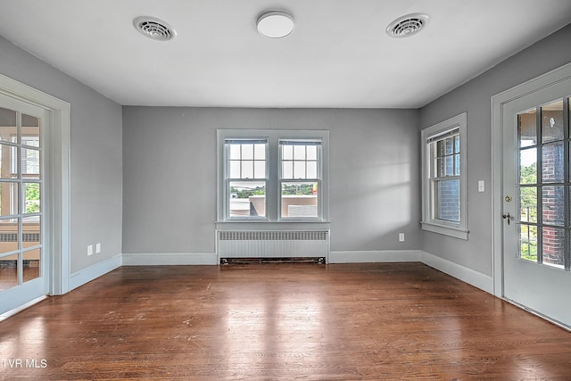 empty room featuring radiator, a wealth of natural light, visible vents, and wood finished floors