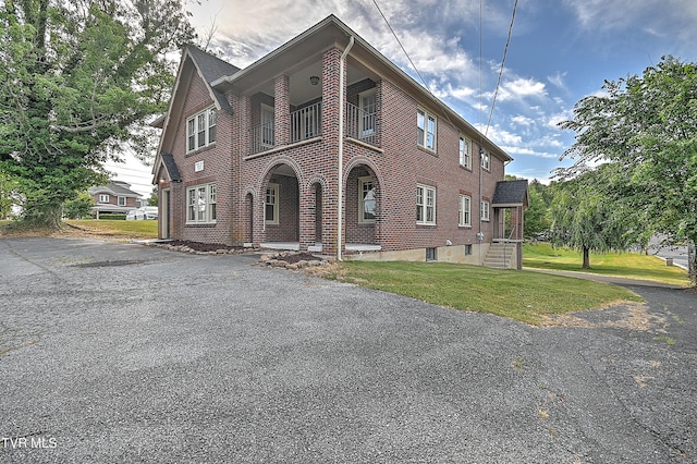 view of front of property featuring a balcony, a front yard, and brick siding