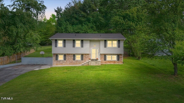 split foyer home featuring a yard, fence, and brick siding