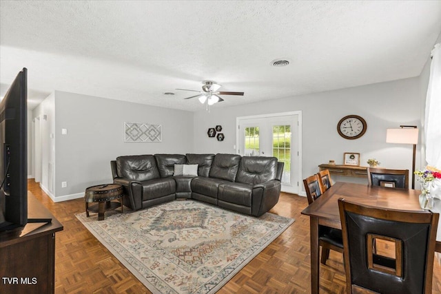 living room with ceiling fan, a textured ceiling, baseboards, and visible vents