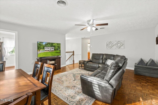 living room featuring a textured ceiling, visible vents, baseboards, and ceiling fan