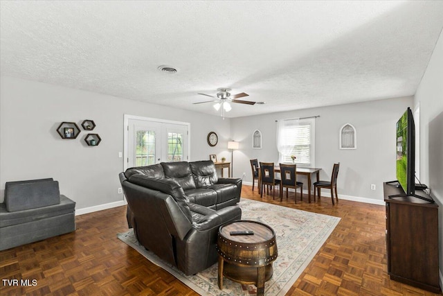 living room with baseboards, visible vents, ceiling fan, and a textured ceiling