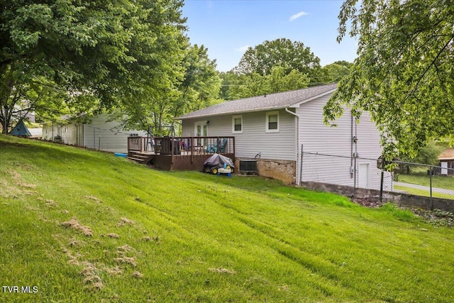 rear view of property featuring a lawn, fence, a wooden deck, and central AC