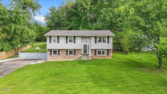 raised ranch with a front lawn, brick siding, and fence
