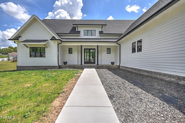 property entrance featuring a yard, board and batten siding, covered porch, and a shingled roof