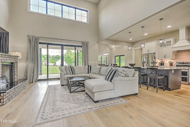 living room with light wood-type flooring, a towering ceiling, a brick fireplace, and recessed lighting