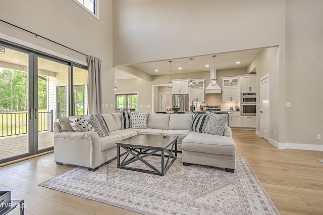 living room with baseboards, light wood finished floors, a towering ceiling, and plenty of natural light