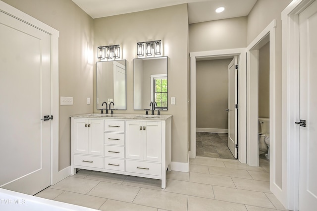 full bathroom featuring a sink, double vanity, toilet, and baseboards