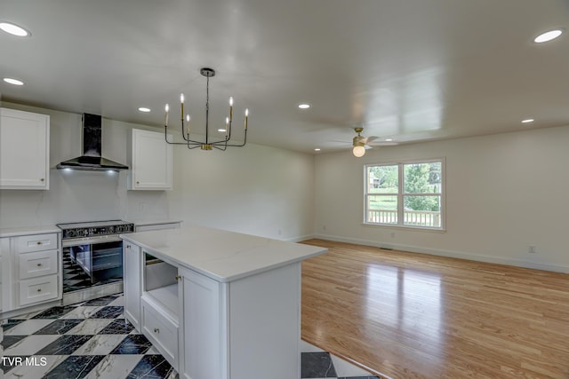 kitchen with wall chimney exhaust hood, ceiling fan, white cabinetry, a kitchen island, and electric stove
