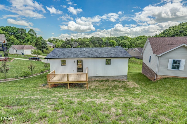 back of property with roof with shingles, a deck, and a lawn