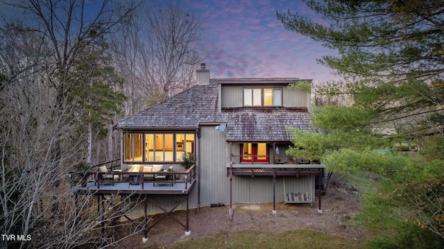 back of property at dusk with a chimney and a deck