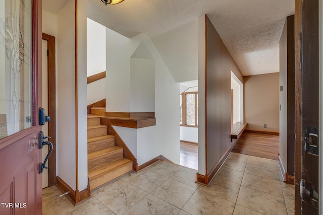 entryway with stairs, a textured ceiling, baseboards, and light tile patterned floors
