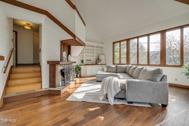 living room with baseboards, a stone fireplace, stairs, high vaulted ceiling, and wood finished floors