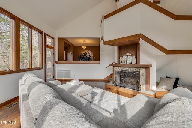 living room featuring wood finished floors, visible vents, vaulted ceiling, a large fireplace, and baseboards