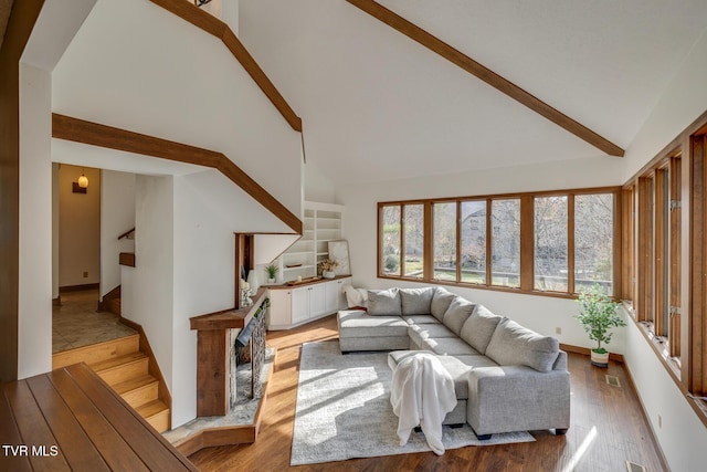 living room with high vaulted ceiling, light wood-type flooring, baseboards, beamed ceiling, and stairs