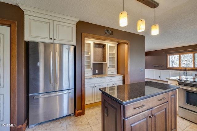 kitchen with dark stone counters, stainless steel appliances, a textured ceiling, visible vents, and decorative light fixtures