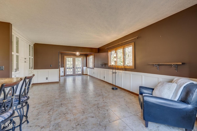 interior space with a decorative wall, french doors, a wainscoted wall, and a textured ceiling