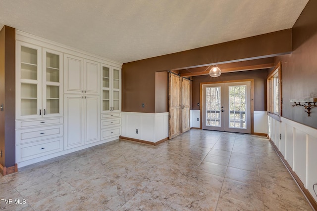 interior space with a decorative wall, french doors, and wainscoting