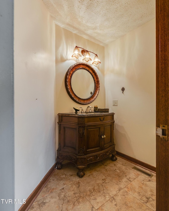 bathroom featuring vanity, a textured ceiling, baseboards, and visible vents