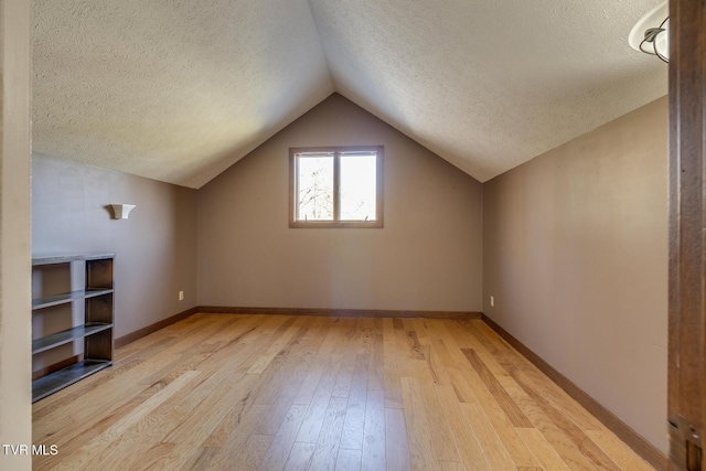 additional living space featuring a textured ceiling, vaulted ceiling, baseboards, and light wood-style floors