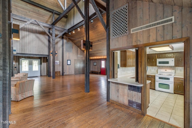 interior space with light wood-type flooring, wooden walls, visible vents, and high vaulted ceiling