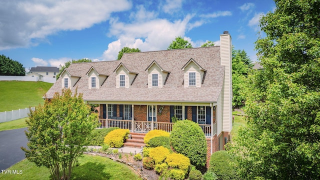 cape cod house with brick siding, a chimney, a shingled roof, and covered porch