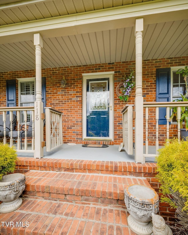 doorway to property with covered porch and brick siding