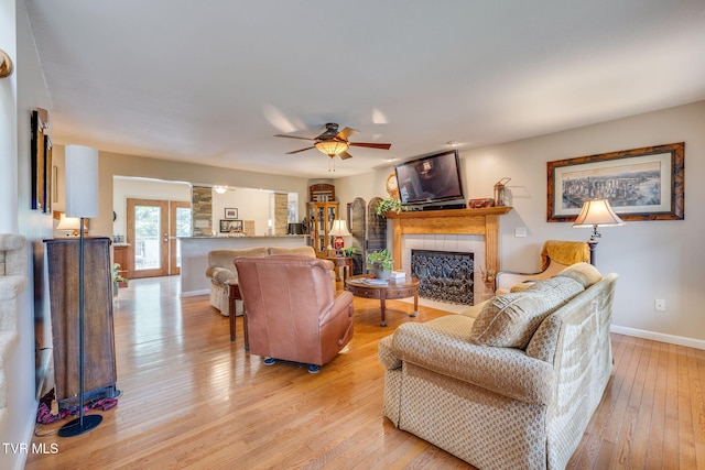 living room with light wood-type flooring, baseboards, a tiled fireplace, and ceiling fan