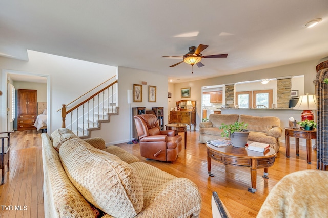 living area with light wood-type flooring, ceiling fan, and stairway