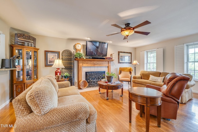 living room with light wood-type flooring, a tiled fireplace, and a ceiling fan