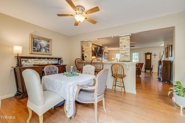 dining space with light wood-style flooring, baseboards, ceiling fan, and ornate columns