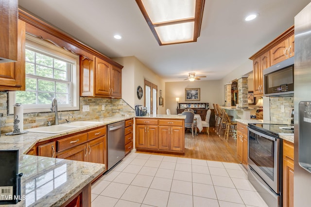 kitchen with appliances with stainless steel finishes, a sink, a peninsula, a ceiling fan, and tasteful backsplash