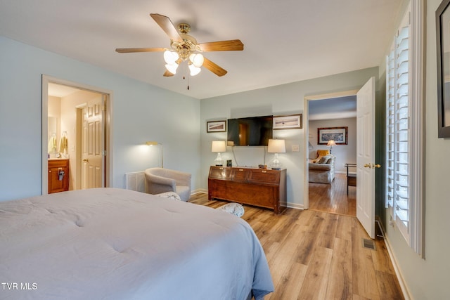 bedroom featuring light wood finished floors, baseboards, ensuite bathroom, and a ceiling fan