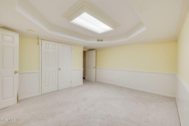 unfurnished bedroom featuring a tray ceiling, carpet flooring, ornamental molding, a closet, and wainscoting