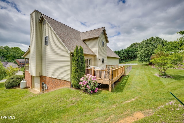 rear view of house featuring a shingled roof, a garage, a wooden deck, a lawn, and a chimney
